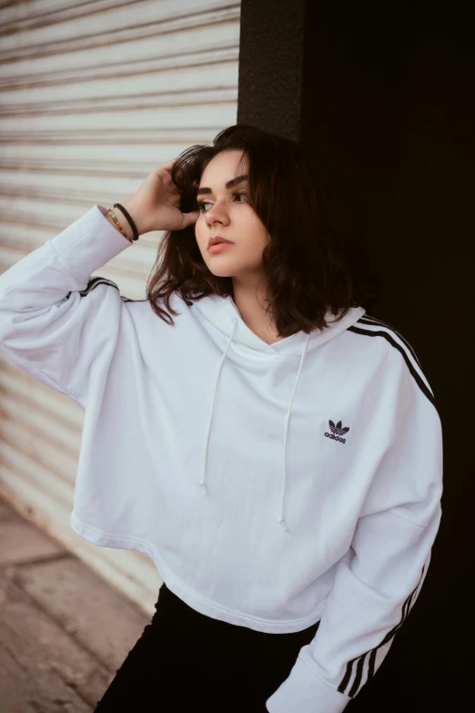 woman in adidas sweatshirt against a wall