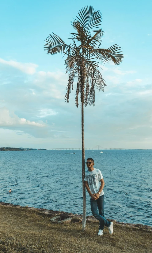 a man leaning on a tree next to the water