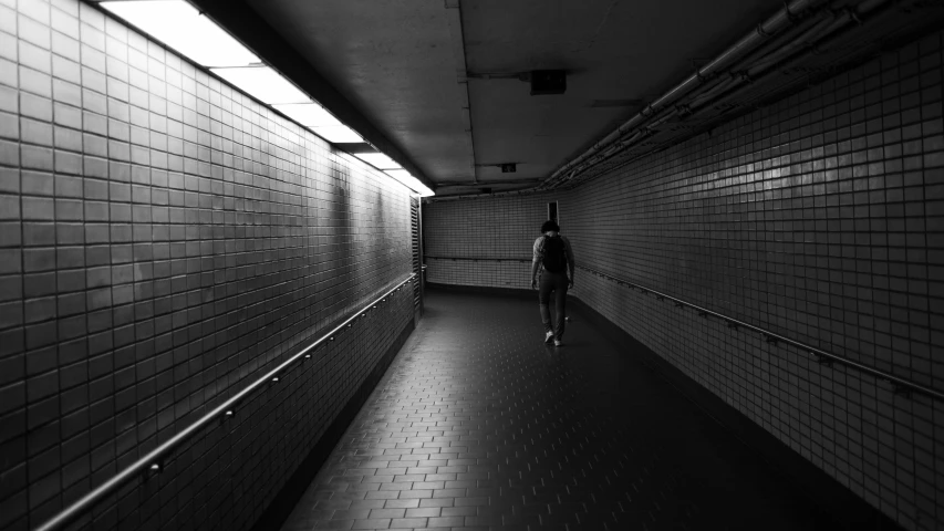 the man walks down a long hallway with tiled walls