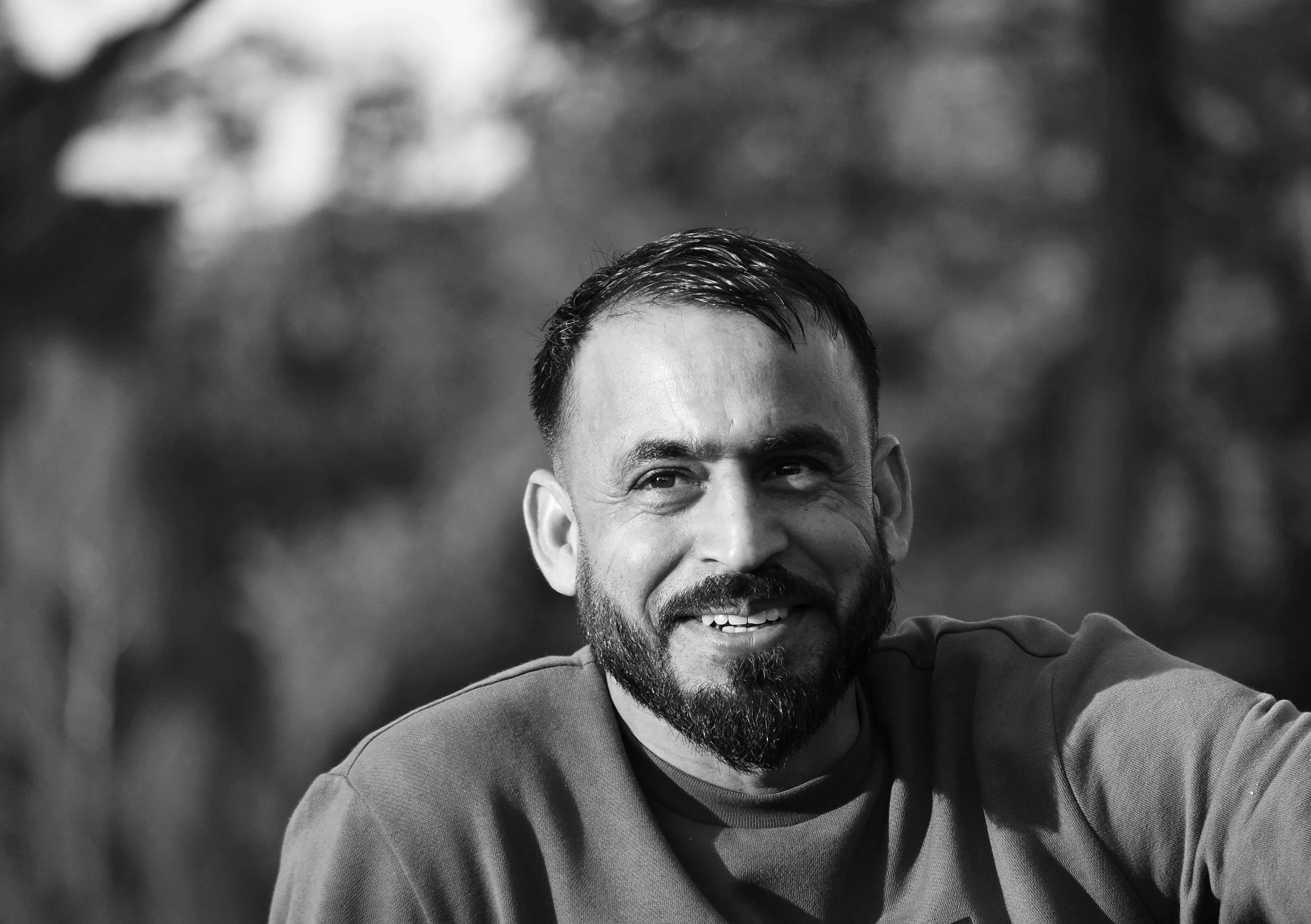 a man with a beard sitting outside and smiling