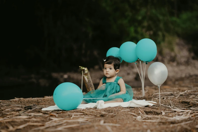 a baby girl sitting on top of grass surrounded by balloons