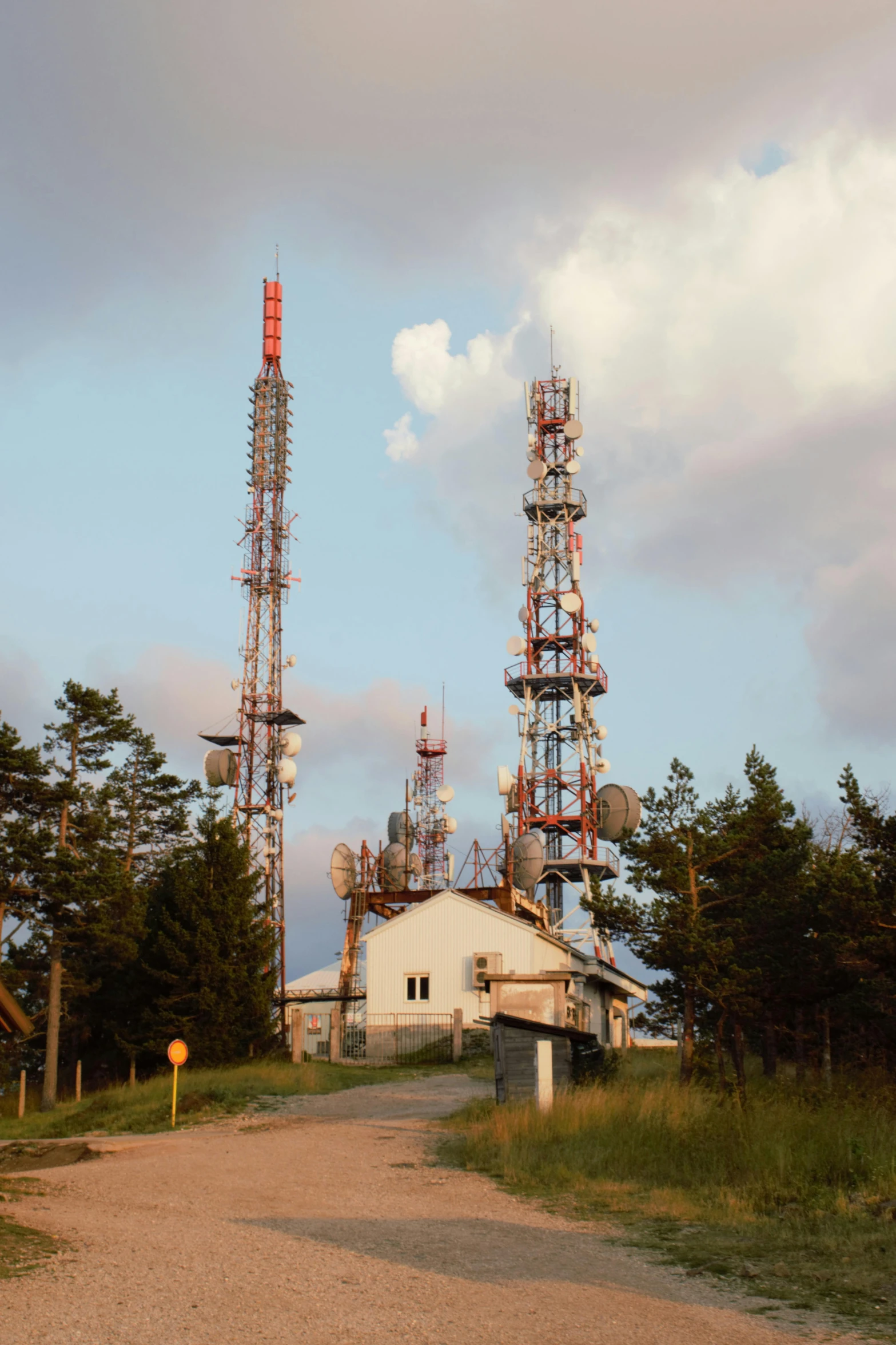 several cell towers near a dirt road on a cloudy day