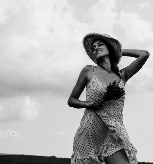 a woman in a white polka dot dress and straw hat holds out a flower