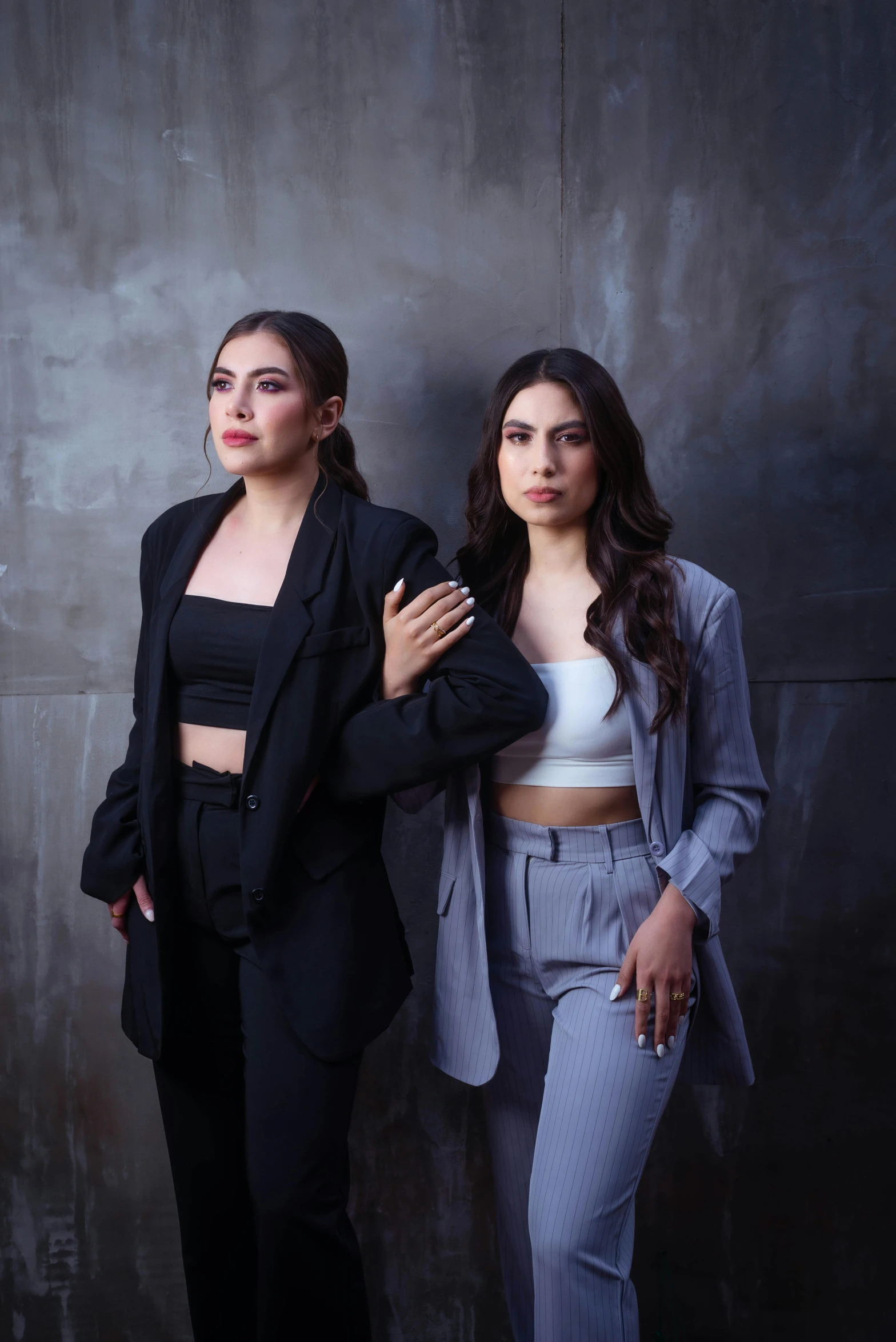 two women stand close together, in front of a black wall