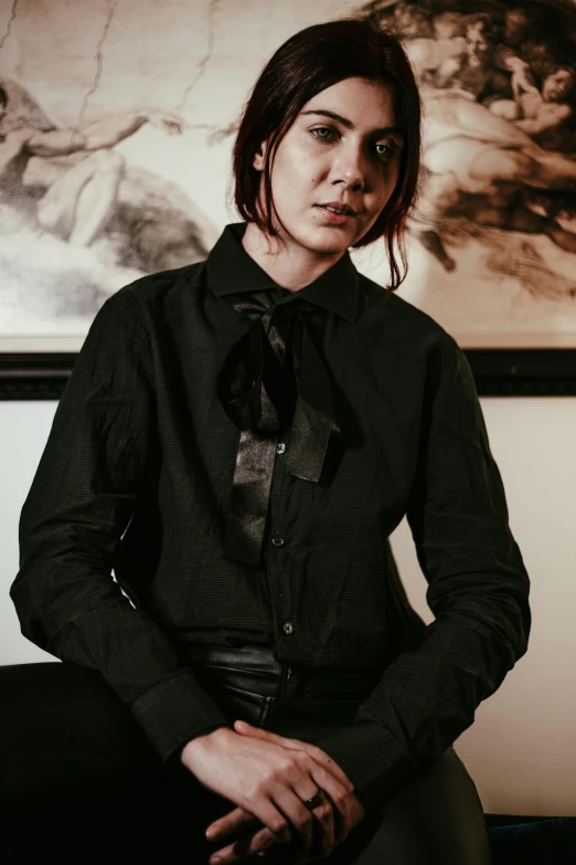 woman with short hair and long dress sitting down in front of a wall art