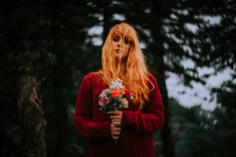 a woman holding a flower standing in the woods