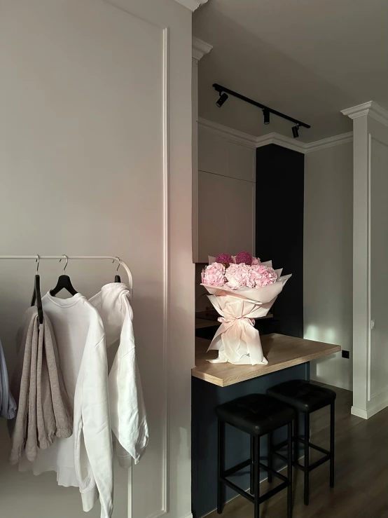 white clothes hanging up on racks and some pink flowers in a vase