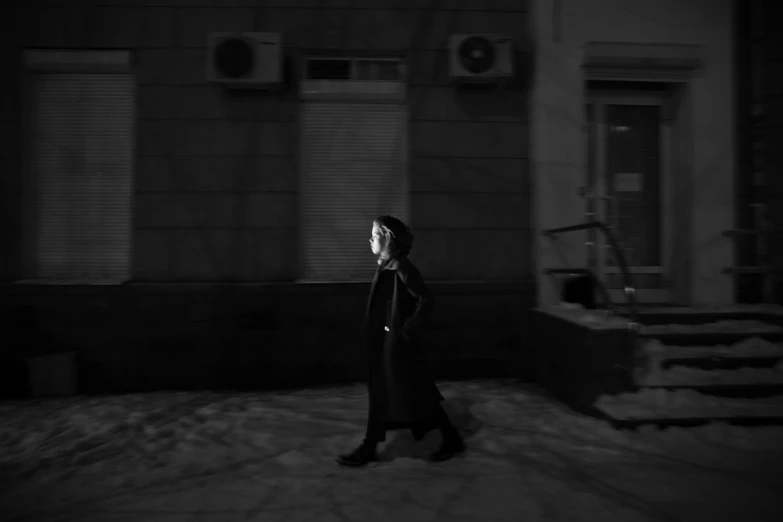 a person in a long black coat walks down a street at night