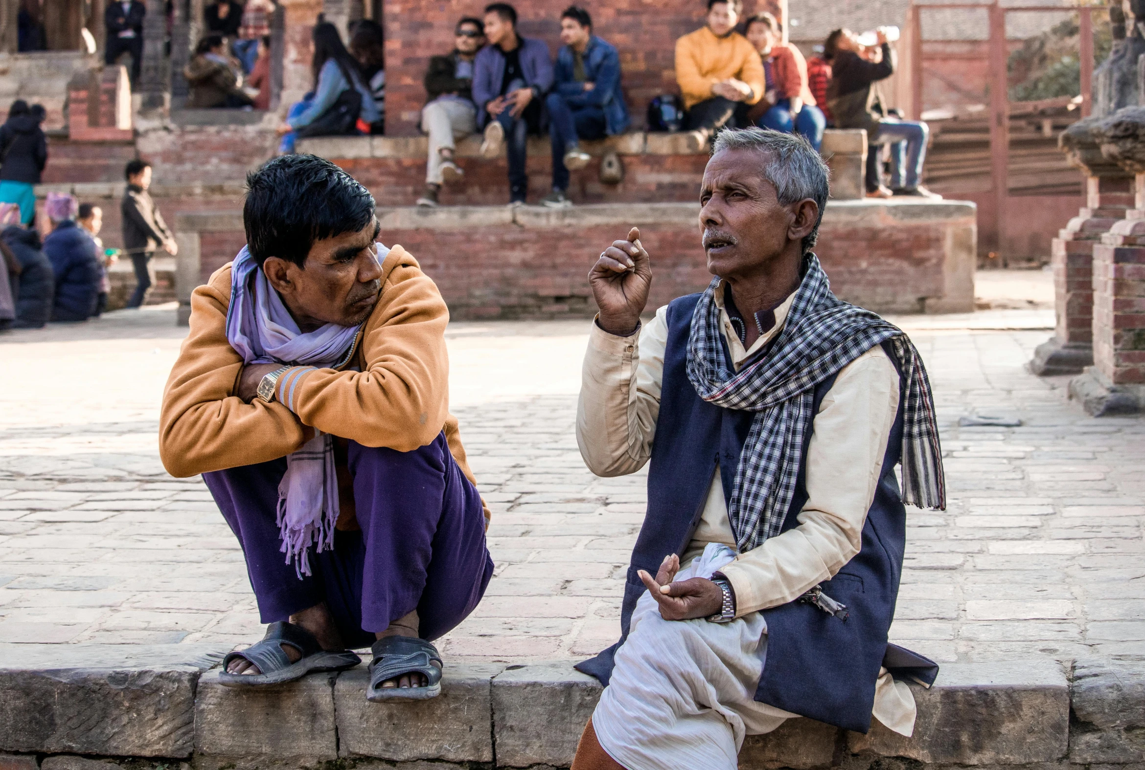 two men sit on a brick wall talking