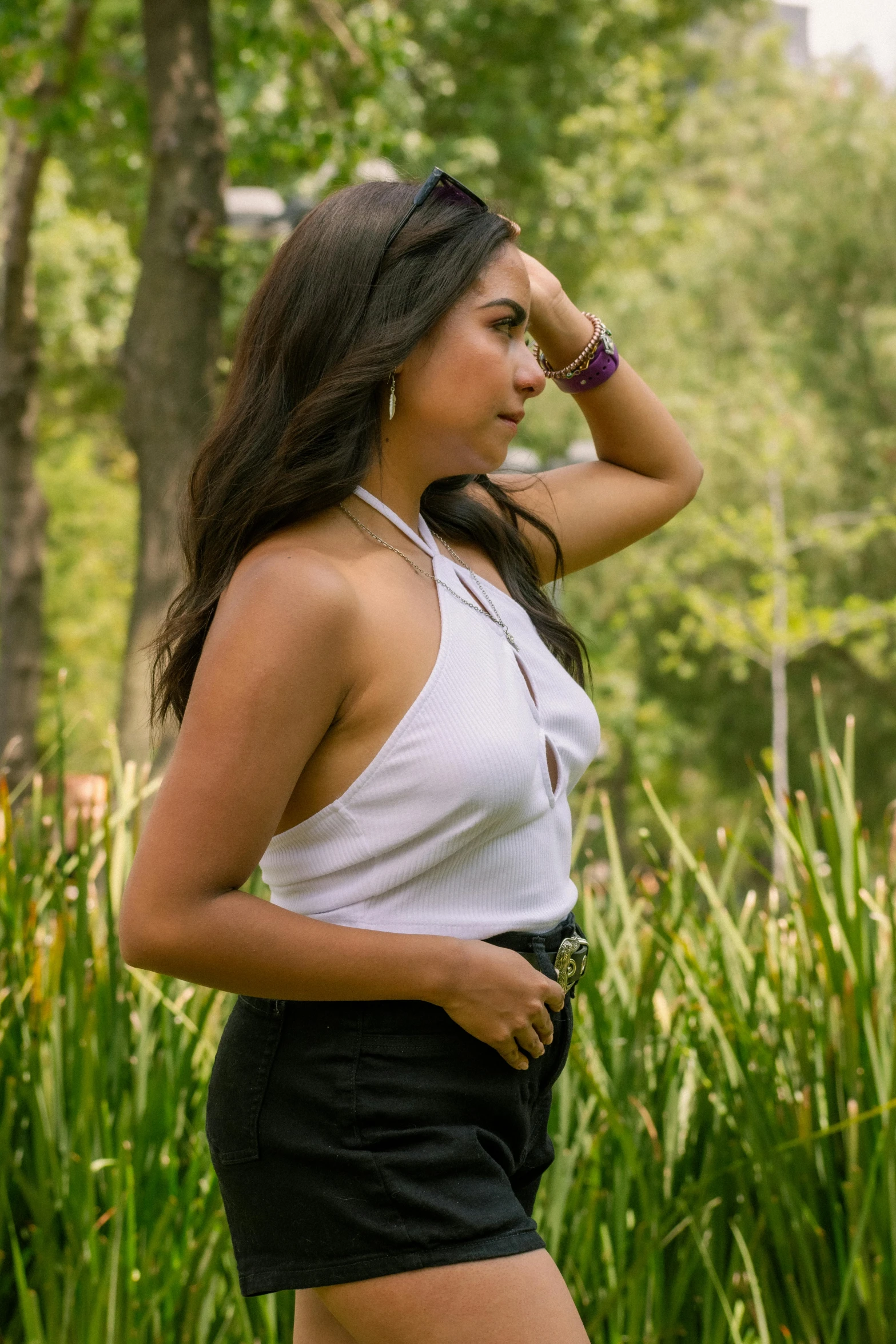 a woman wearing a skirt, white shirt and brown sandals stands in the woods