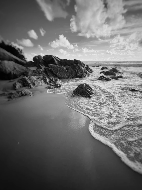 black and white pograph of waves crashing into rocks on beach