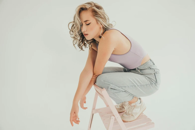 a woman in jeans kneeling down on a pink chair