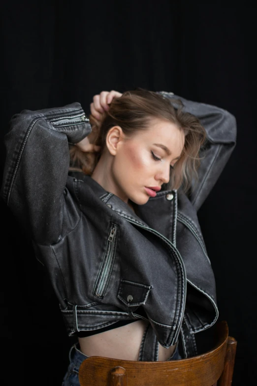 a woman with long hair, wearing a jean jacket, stands against a black background