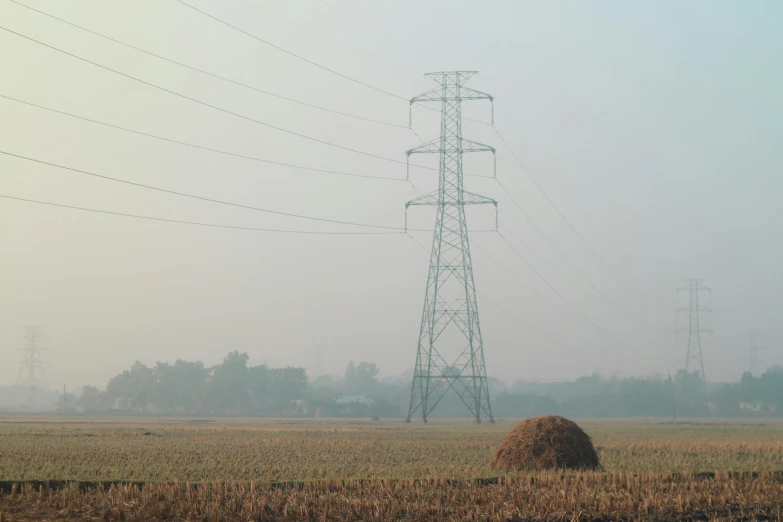 a field with a couple stacks of hay and power lines in the background