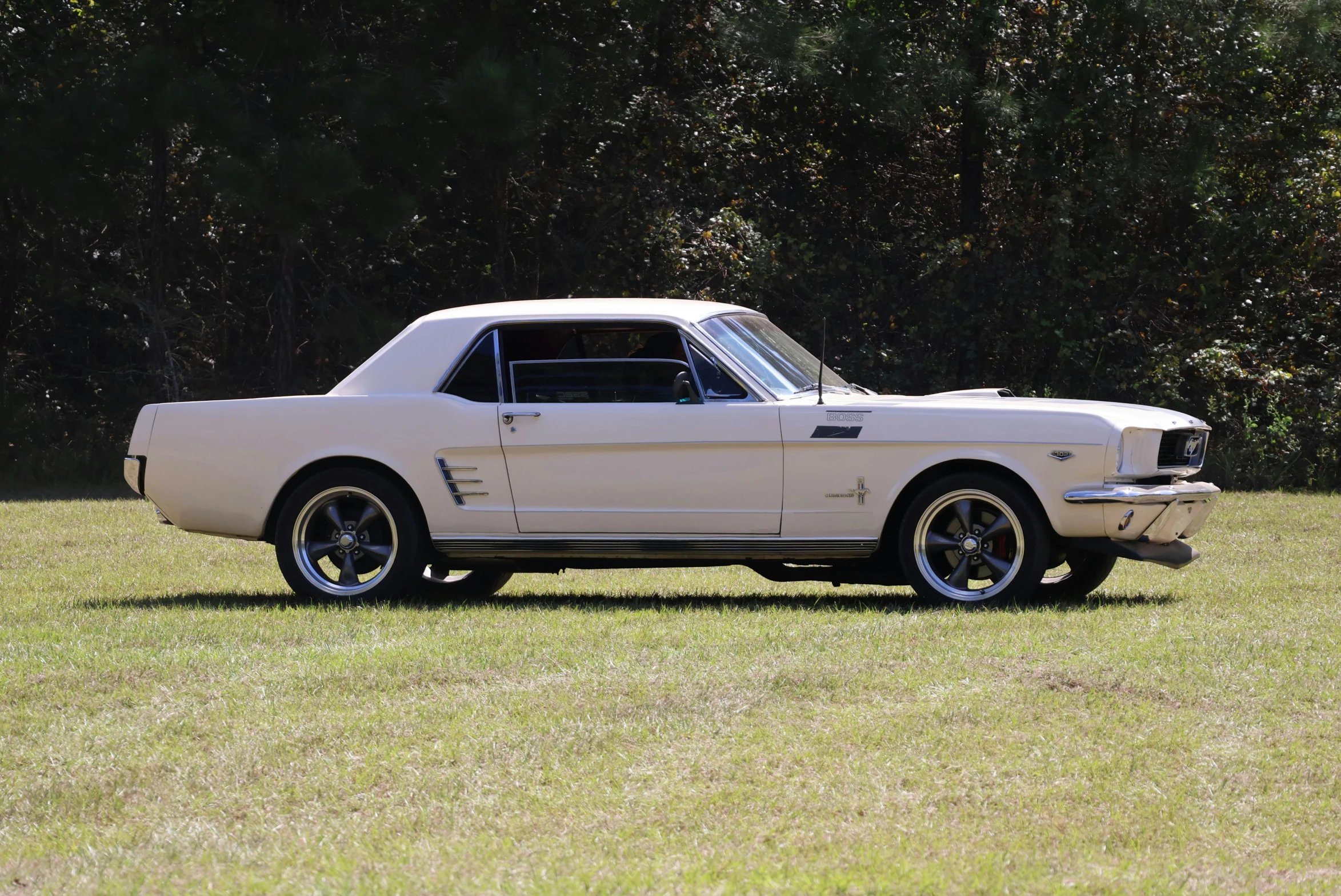 a white vintage mustang muscle car sitting in a field