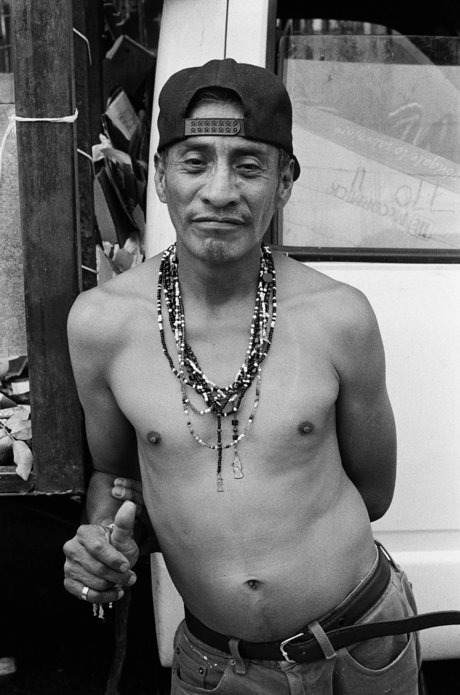 shirtless man standing with a skateboard and wooden rail in background