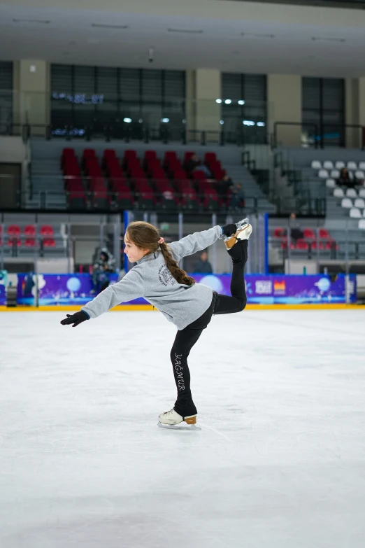 a female figure skater in a gray sweatshirt doing a backhand move