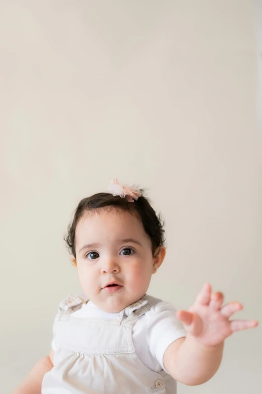 a baby in a white romper holds up her hands to show off