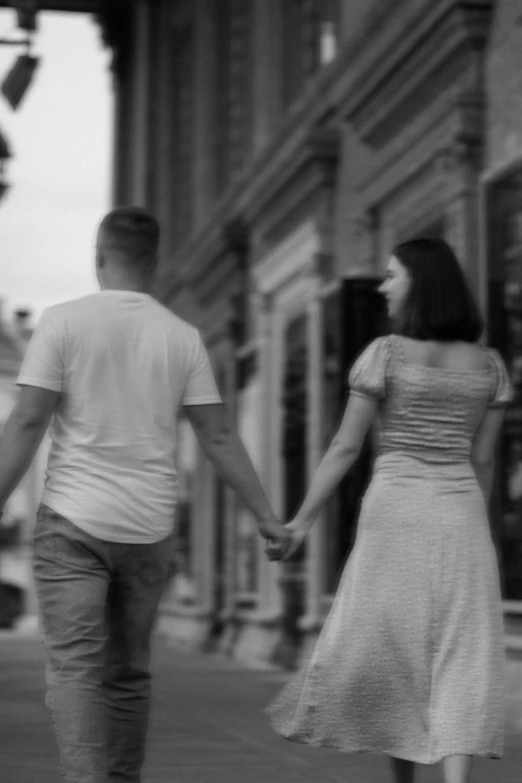 a man and woman holding hands while walking down a street