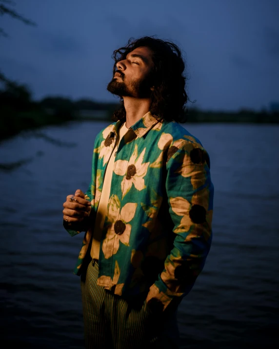 a man standing next to the water with his hair pulled back