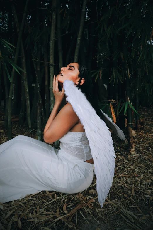 woman wearing an angel costume sitting in front of bamboo trees