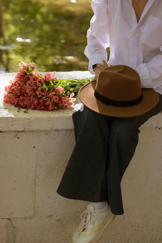 a person with a hat sits on a ledge near flowers