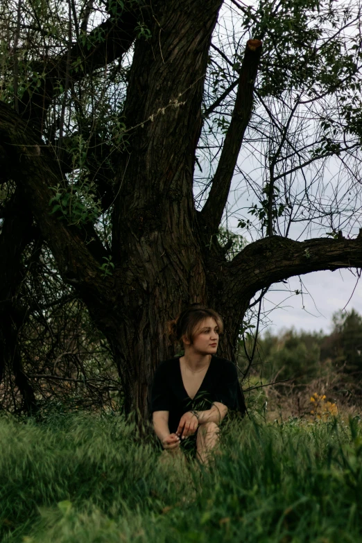 a woman sits beneath a tree looking up at soing