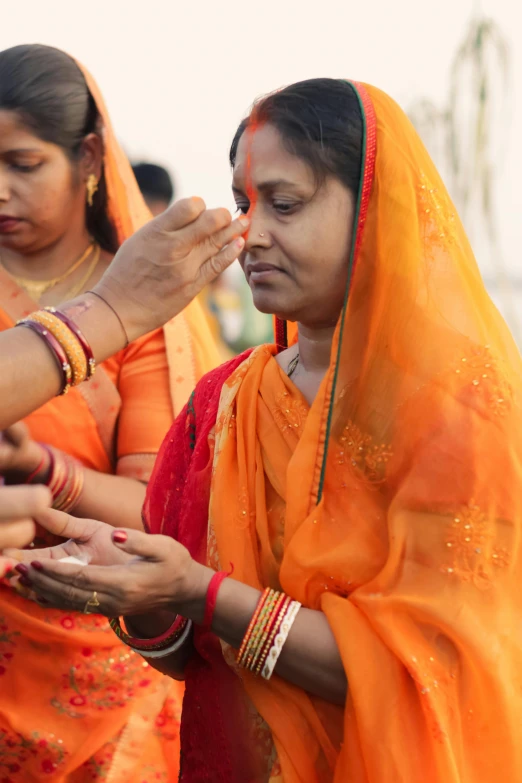 two indian women both wearing orange and some holding their hands together