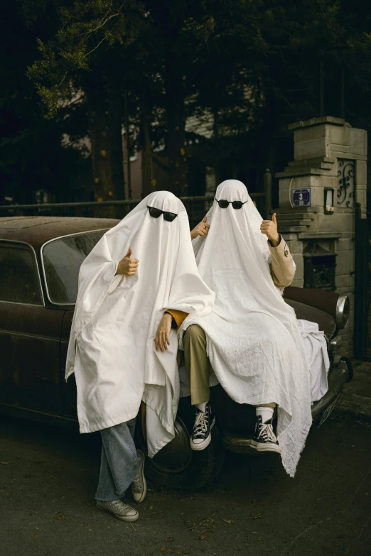 two people in white robes sitting on the hoods of a car