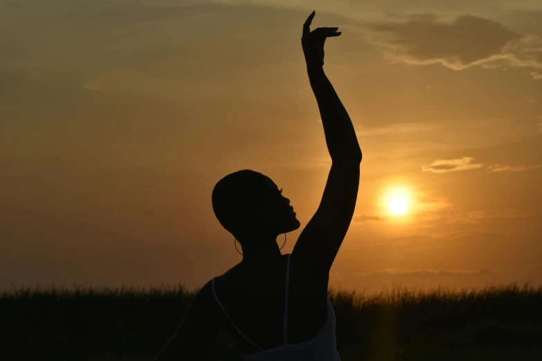a woman standing in a field, arms up as the sun sets