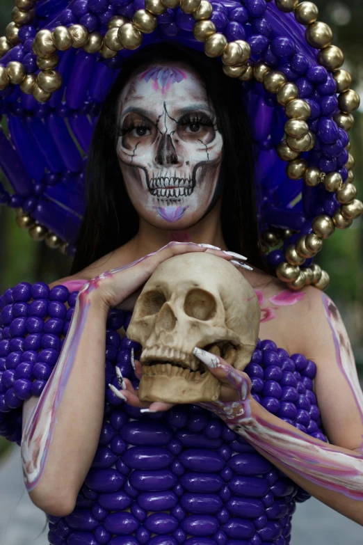 a woman with an artistically decorated makeup holds a skull