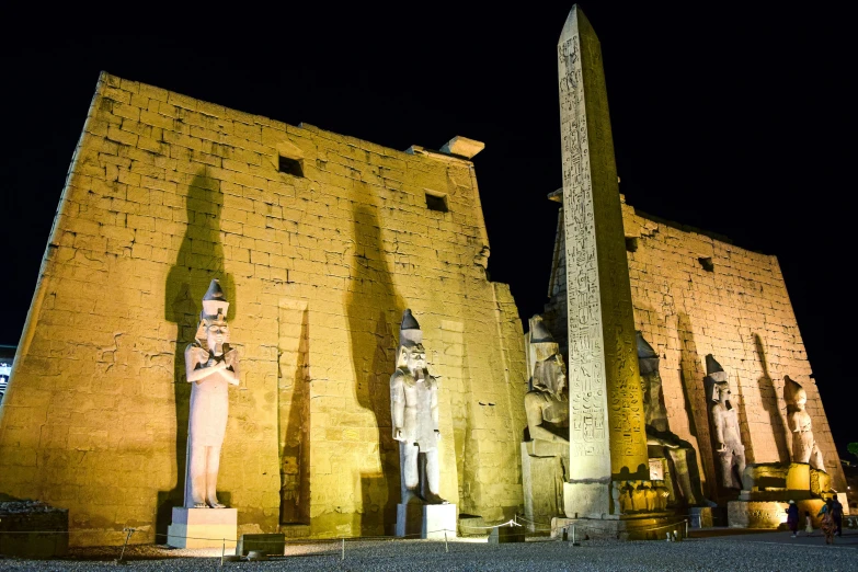 two statues stand in front of the obelisk of an ancient temple at night