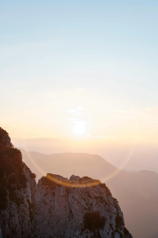 the sun sets over mountains with large rocks in the foreground