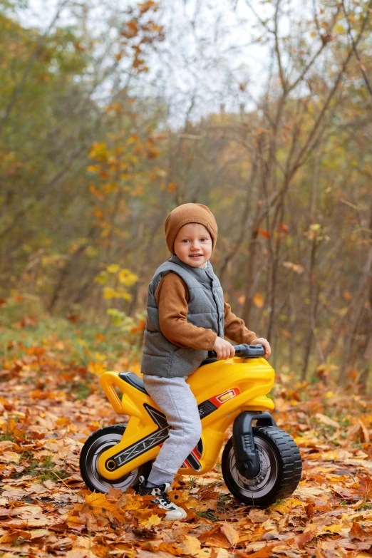 a boy sitting on his little yellow bike in a pile of autumn leaves