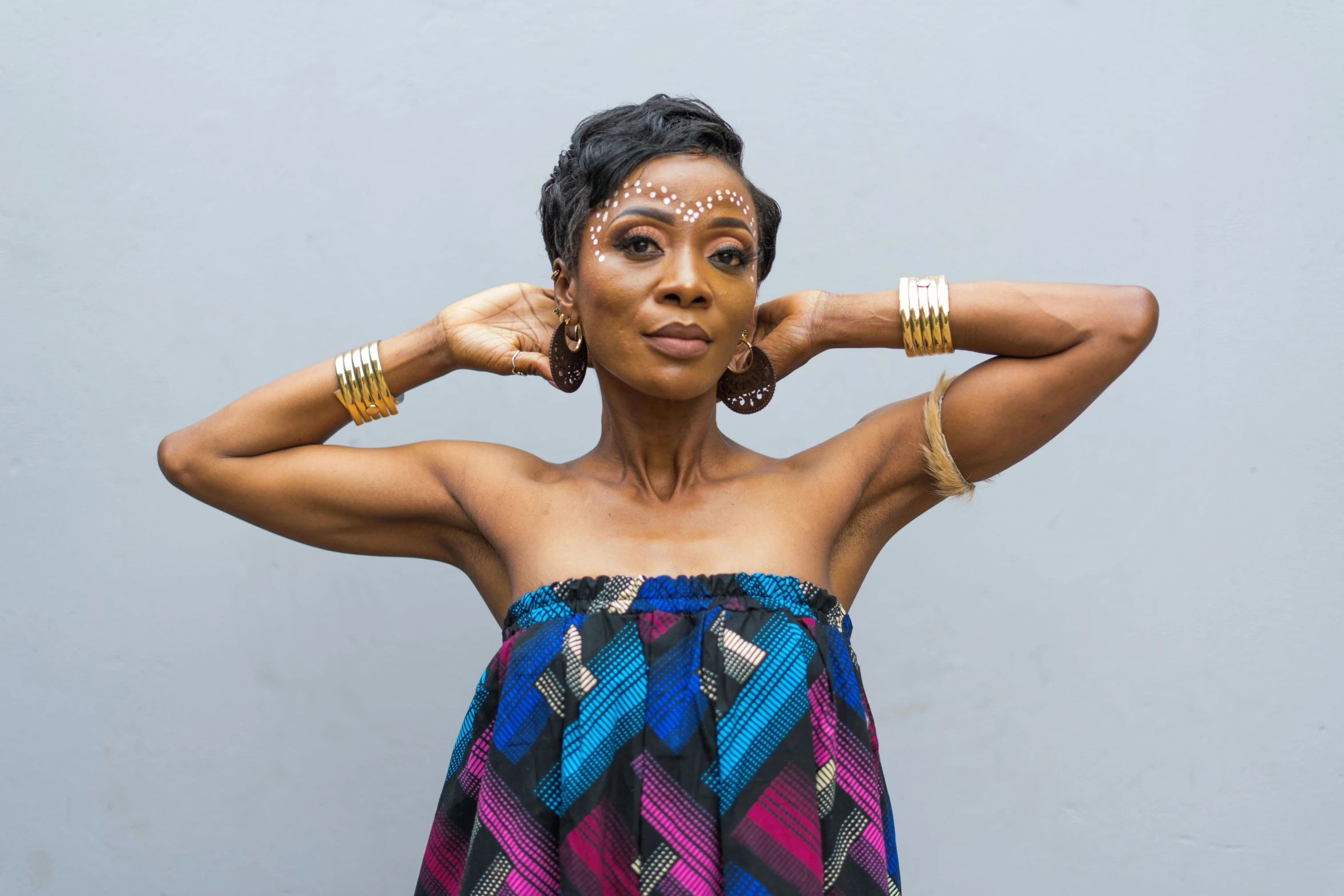 a black woman with painted face and celets standing in front of a grey wall