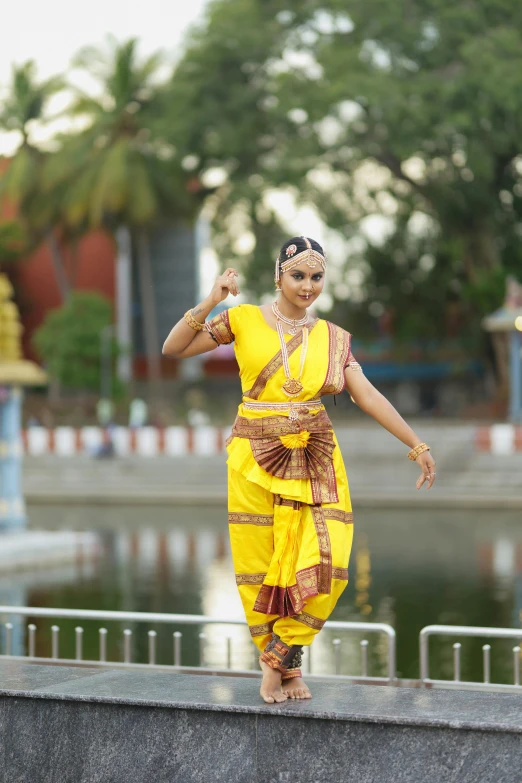 a woman in yellow dress posing by a lake