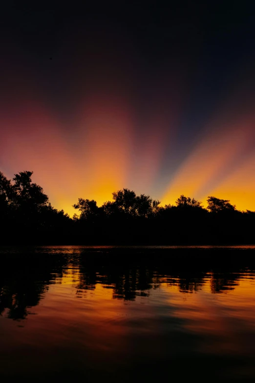 a sunset over the trees reflecting in a lake