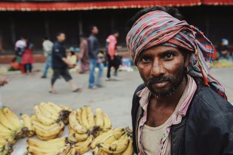 a man wearing a head scarf is next to bunches of bananas