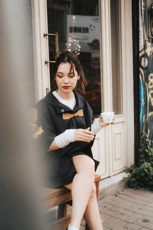 woman sitting on bench outside of store holding coffee