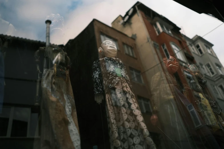 a window display with some glass mannequins and building behind them