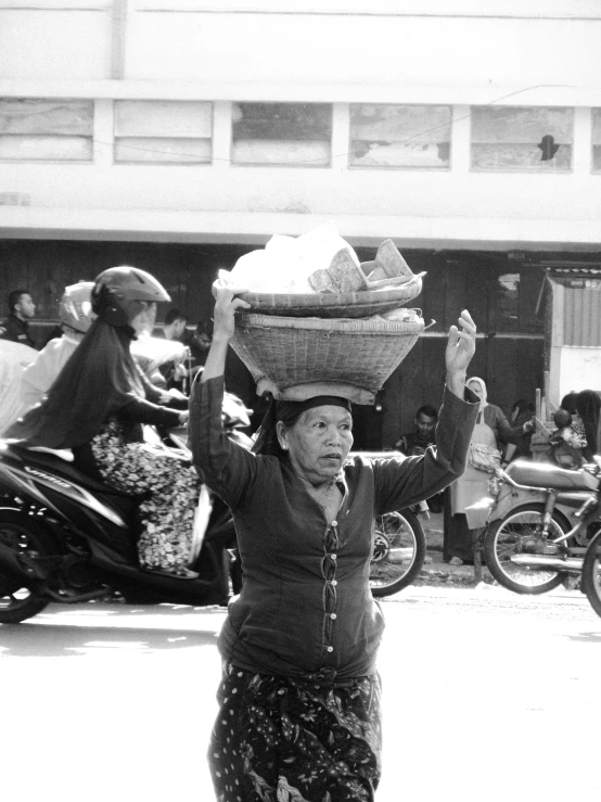 an older woman carrying some things on her head in the street