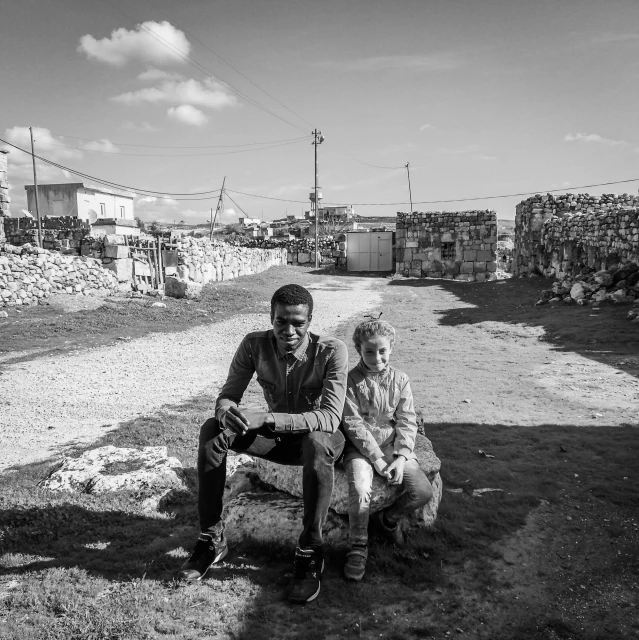 two people are sitting on the rock next to the village