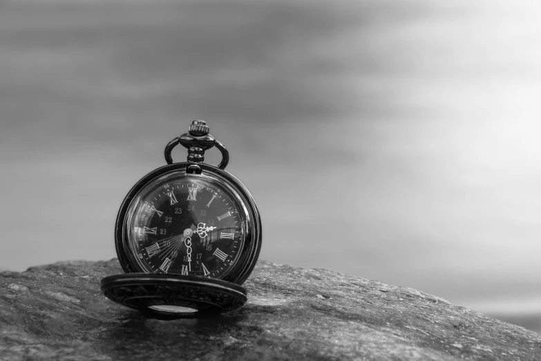 an old pocket watch with roman numerals sits on a rock