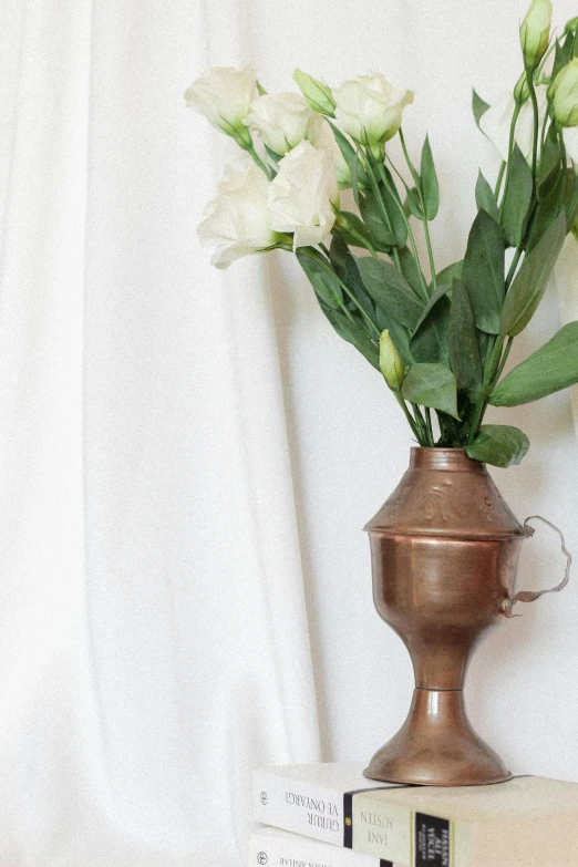 a metal container sitting on a book and two white flowers in it