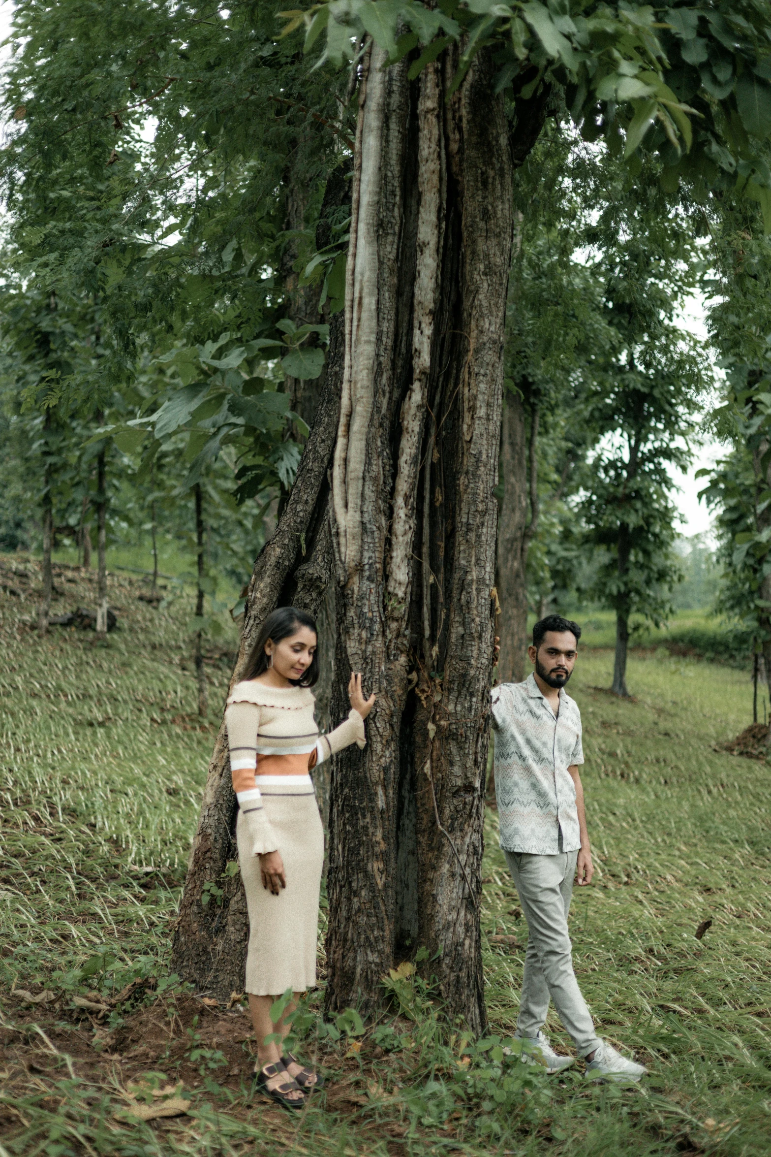 two young people standing by a tree on a green grass covered field