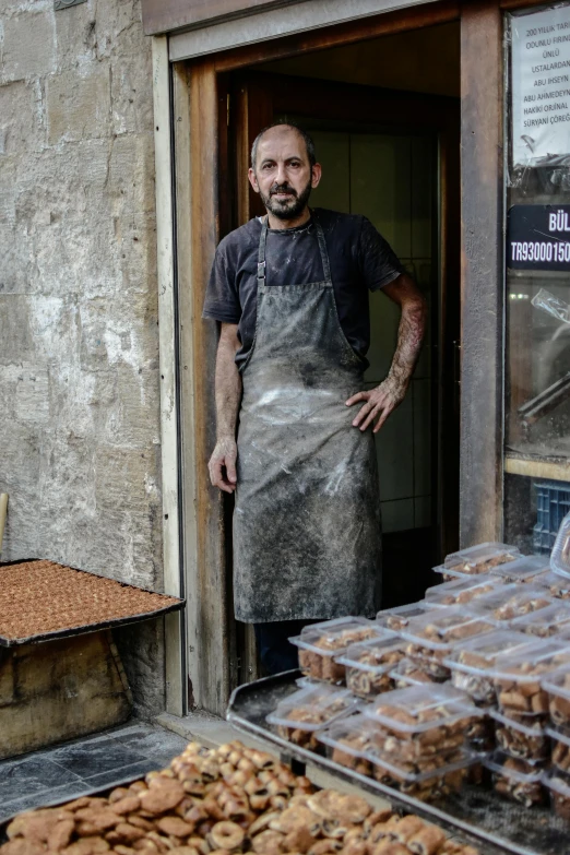 a man stands outside of a bakery while wearing an apron