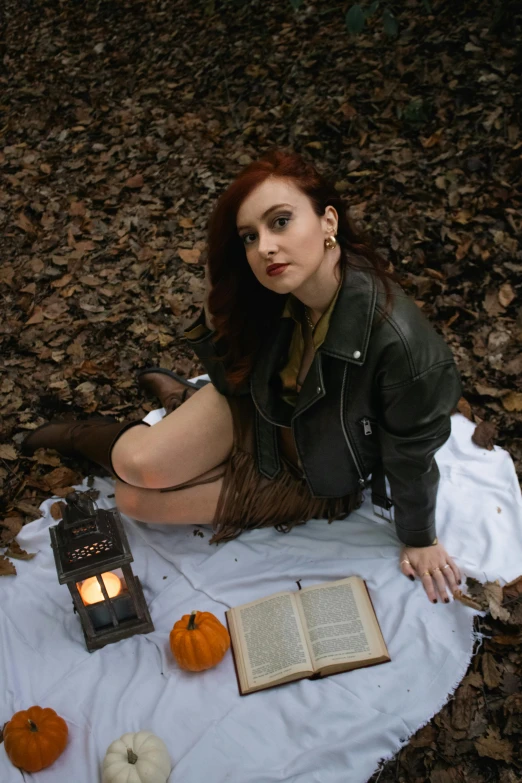 a woman sitting on a blanket in the forest with an open book and a lantern