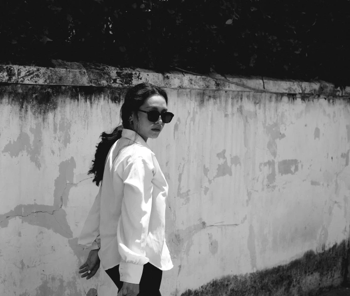 a woman walking past a wall with sunglasses on