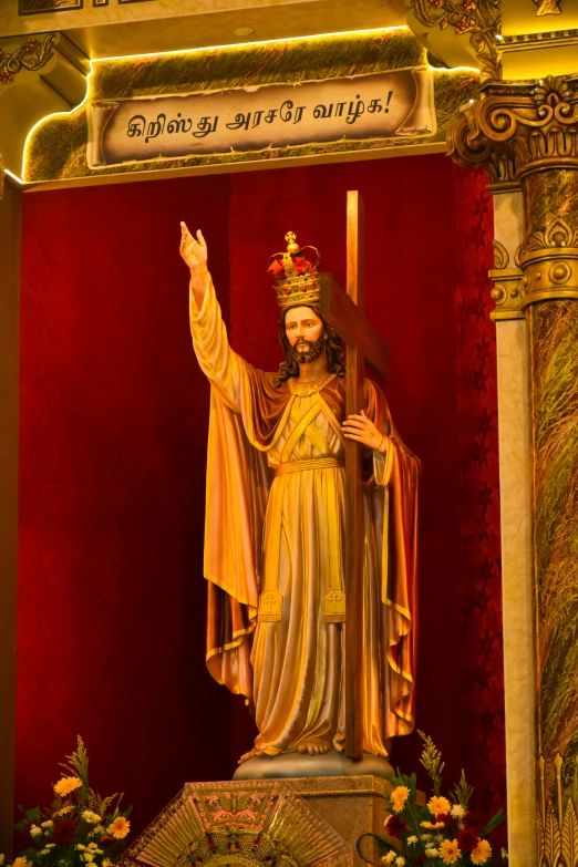 a statue of jesus holding a cross in front of a red wall