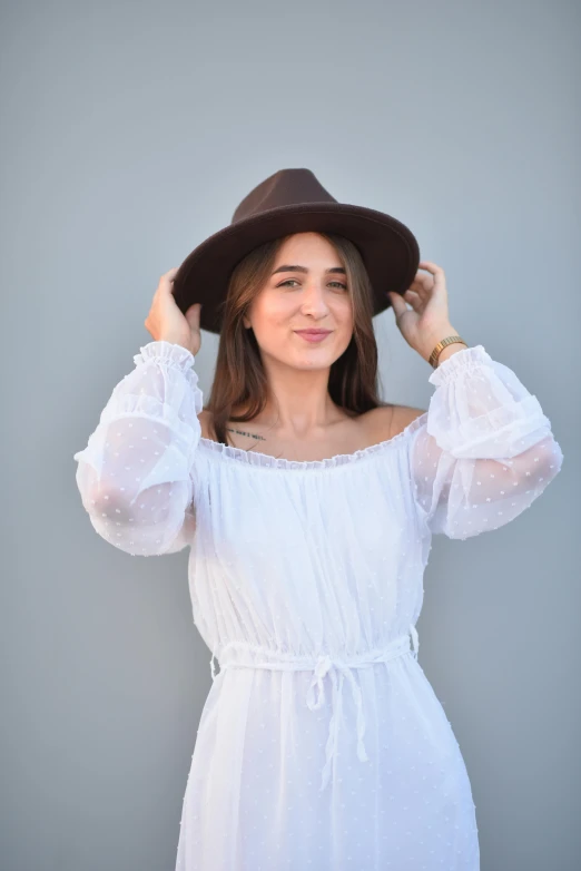 a woman wearing a white dress, a hat and holding her hands on her head